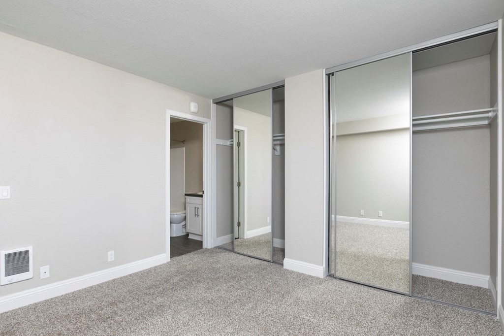 an empty bedroom with mirrored closet doors and a bathroom