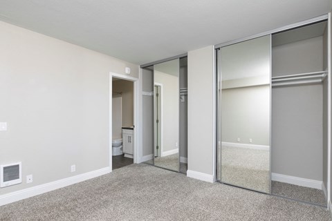 an empty bedroom with mirrored closet doors and a bathroom