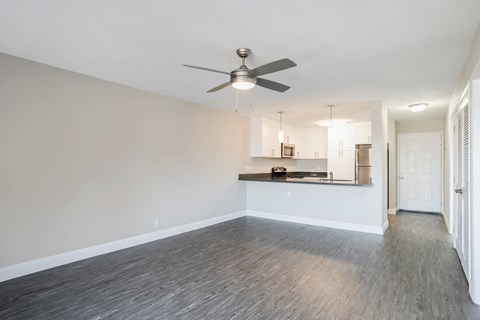 an empty living room with a ceiling fan and a kitchen