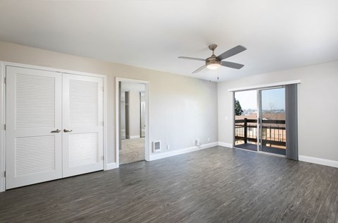 an empty living room with a ceiling fan and a door to a balcony