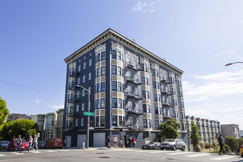 A large building with a blue facade is surrounded by cars and people.