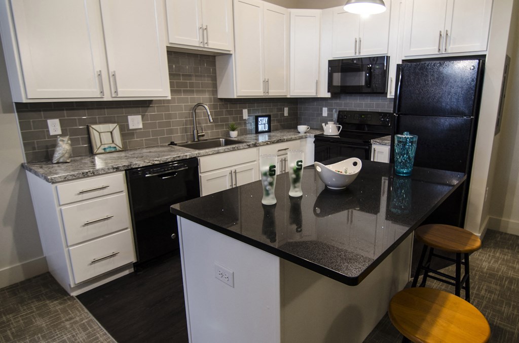 a kitchen with black countertops and white cabinets and a black refrigerator