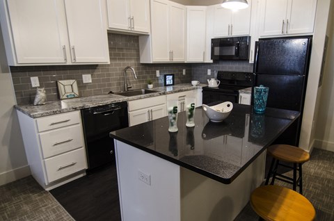 a kitchen with white cabinets and black counter tops and a black refrigerator