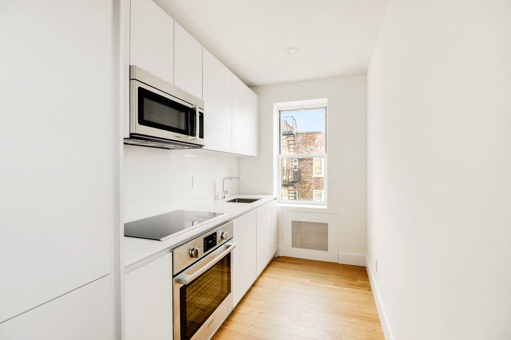 A kitchen with white cabinets and a window.