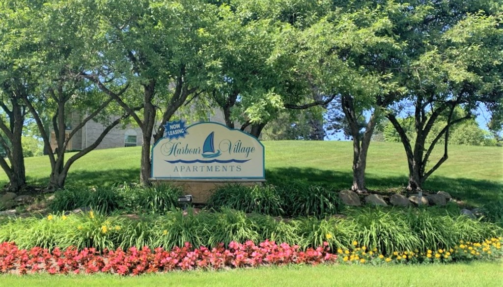 the sign in front of a park with trees and flowers