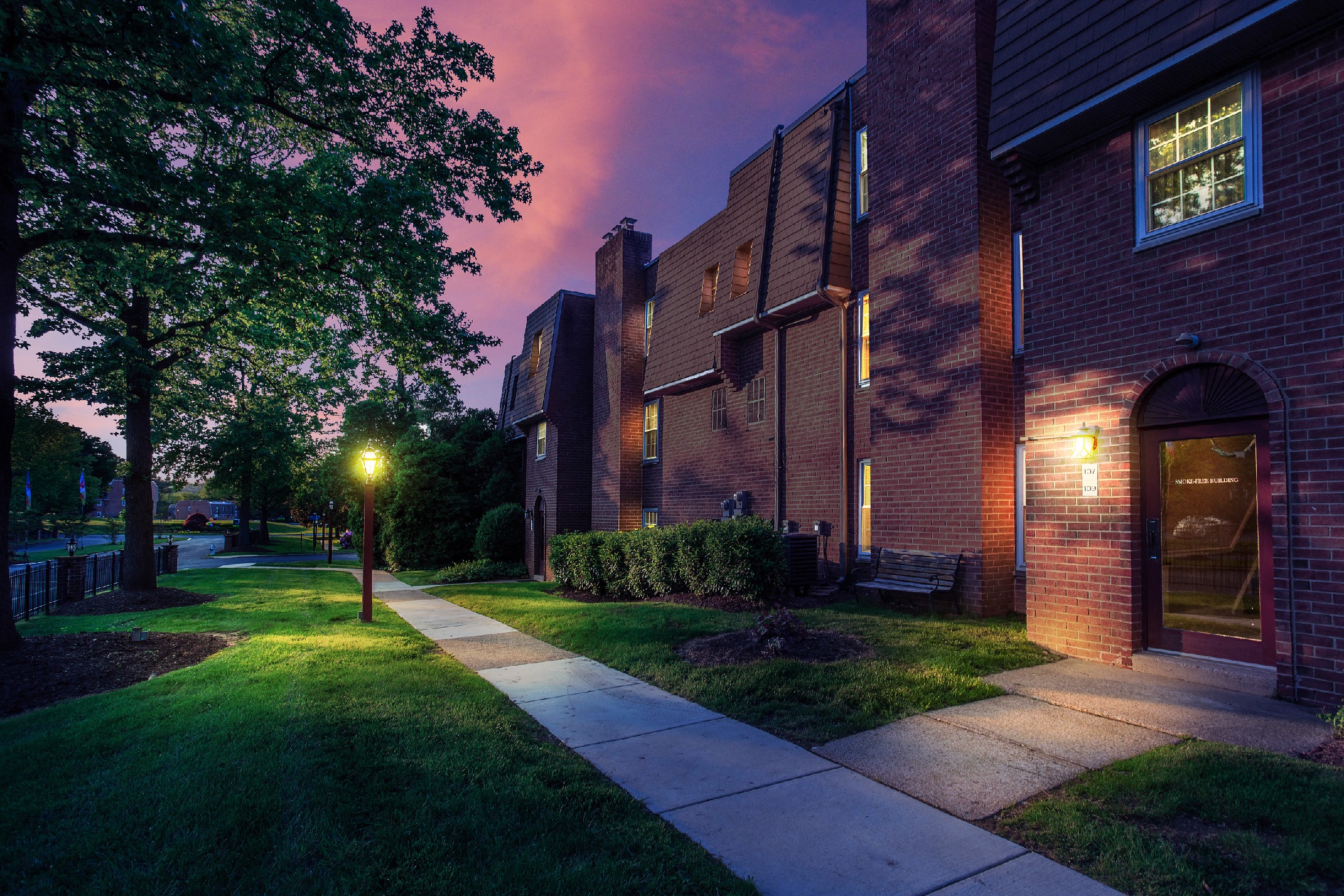 Exterior of one of the buildings at night, showing landscaped grass, hedges, and walkway