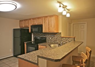 Kitchen with granite countertop, black appliances, and a black and beige tile backsplash