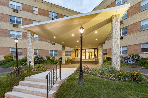 Exterior of a building showing entryway with awning behind two flower beds.