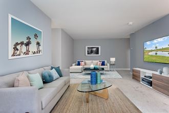 Model furnished living room with gray walls and carpet, opened to family room. - Photo Gallery 4