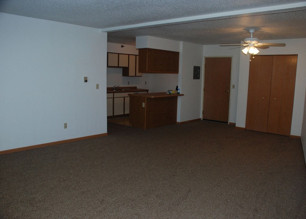 an empty living room and kitchen with a ceiling fan