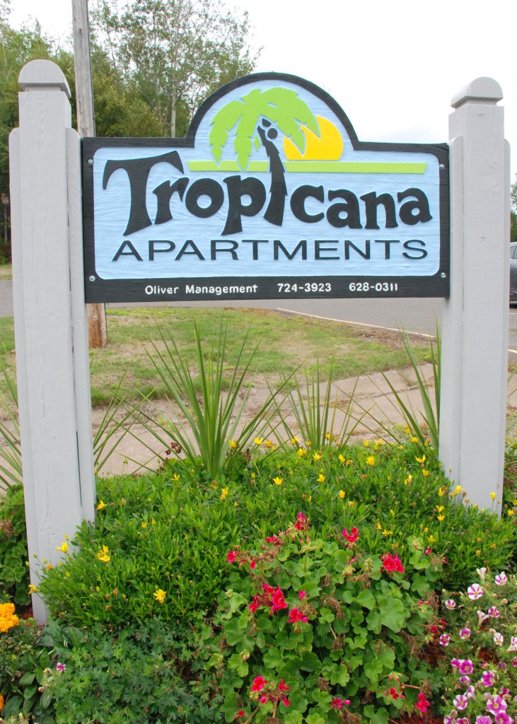 a sign for tropicana apartments in front of flowers