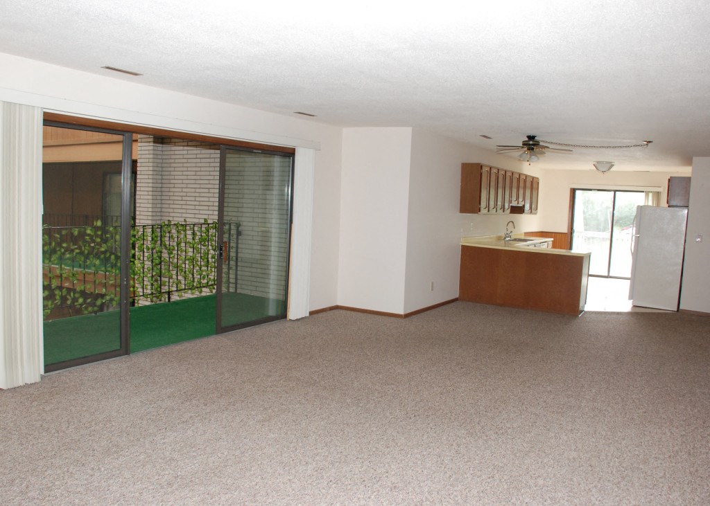 an empty living room with a kitchen and a sliding glass door