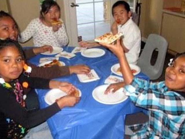 a group of children sitting at a table eating pizza