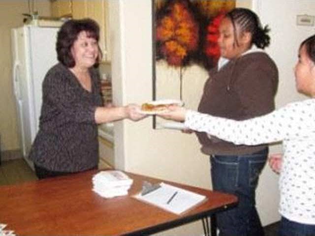 a woman handing another woman a piece of pizza