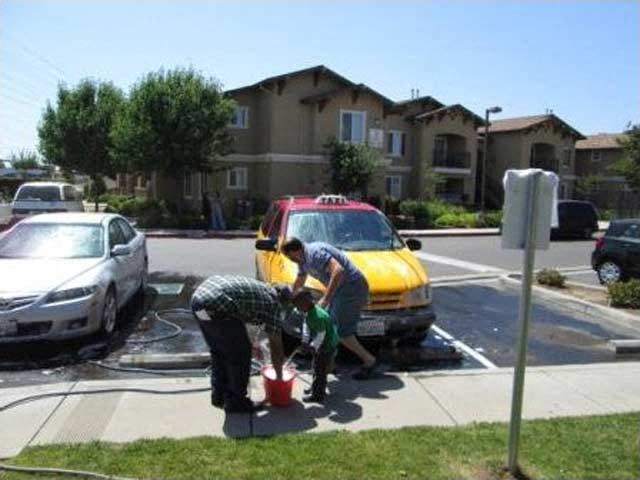 two people are watering a fire hydrant in front of a yellow car