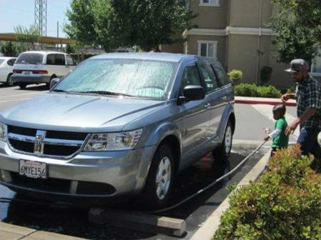 a man and two children washing a car with a hose