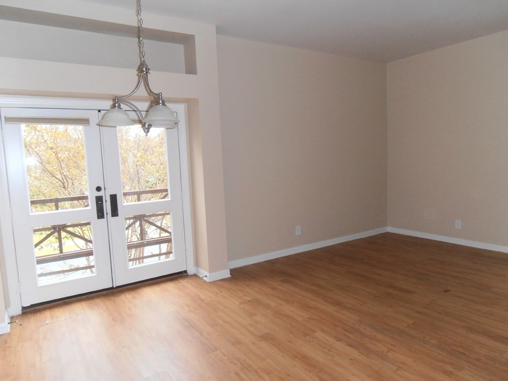 an empty living room with a wooden floor and a door to a balcony