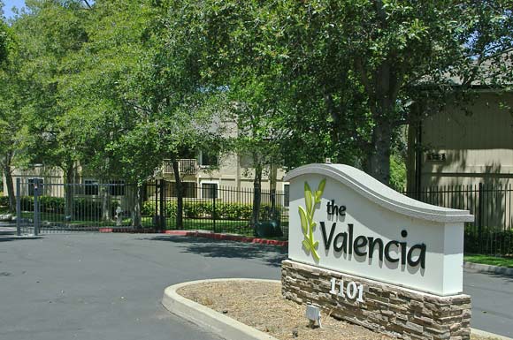 a sign for the apartments in front of a fence and trees