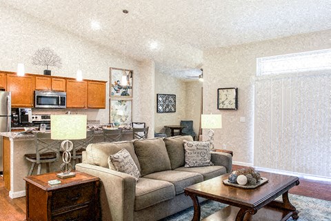 A living room with a couch, a coffee table, and a kitchen area in the background.