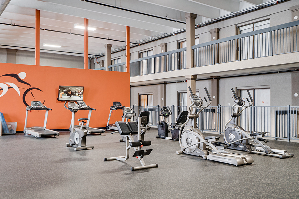 large fitness room with lots of equipment and orange wall