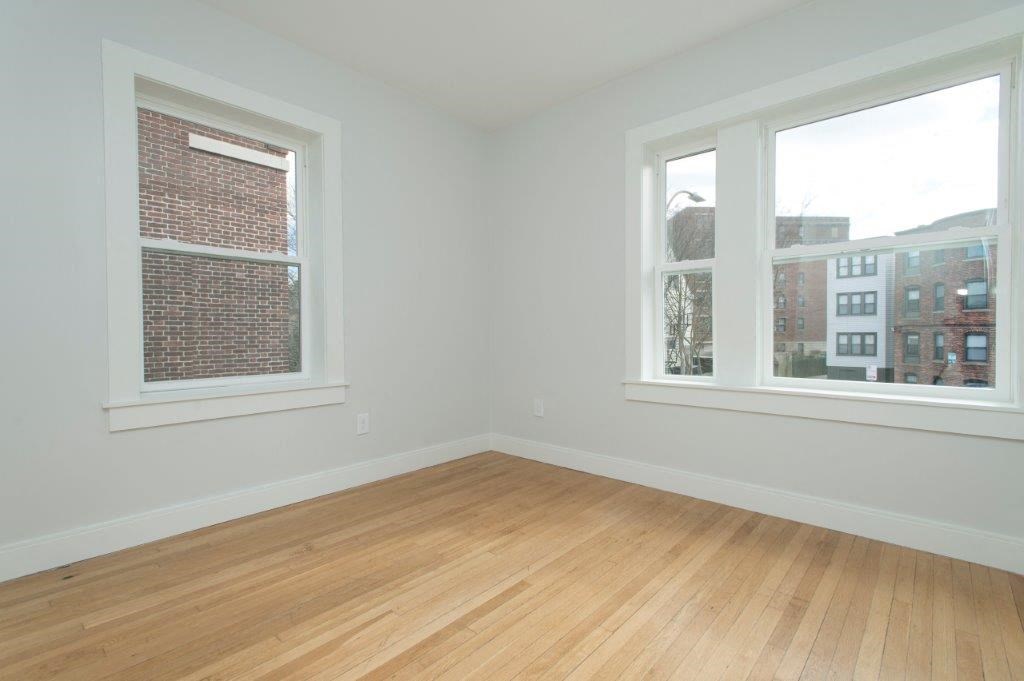 an empty room with two windows and a wooden floor
