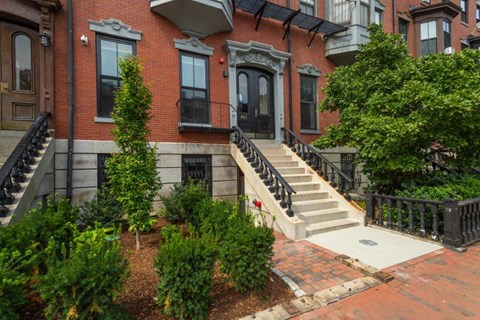 the front of a red brick house with stairs and a garden