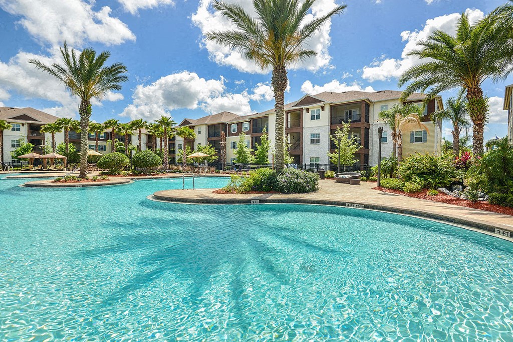 A swimming pool in front of apartment buildings with palm trees at Cabana Club Apartments, Jacksonville, FL