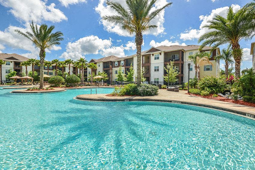 a large swimming pool with palm trees in front of an apartment building