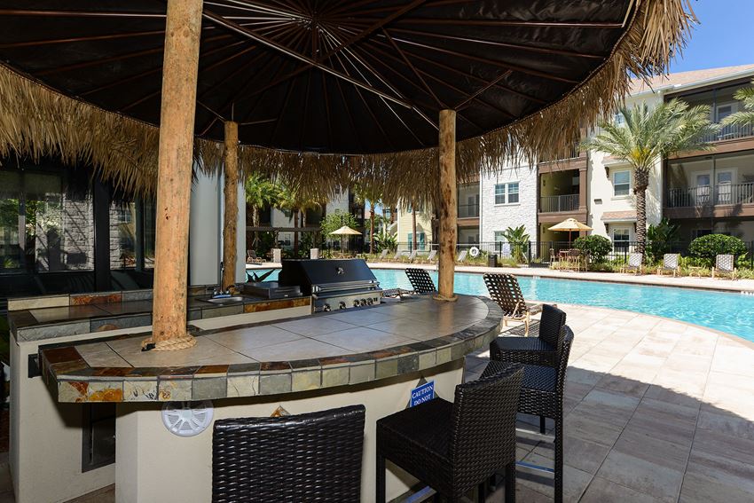 a bar and seating area under an umbrella next to a swimming pool