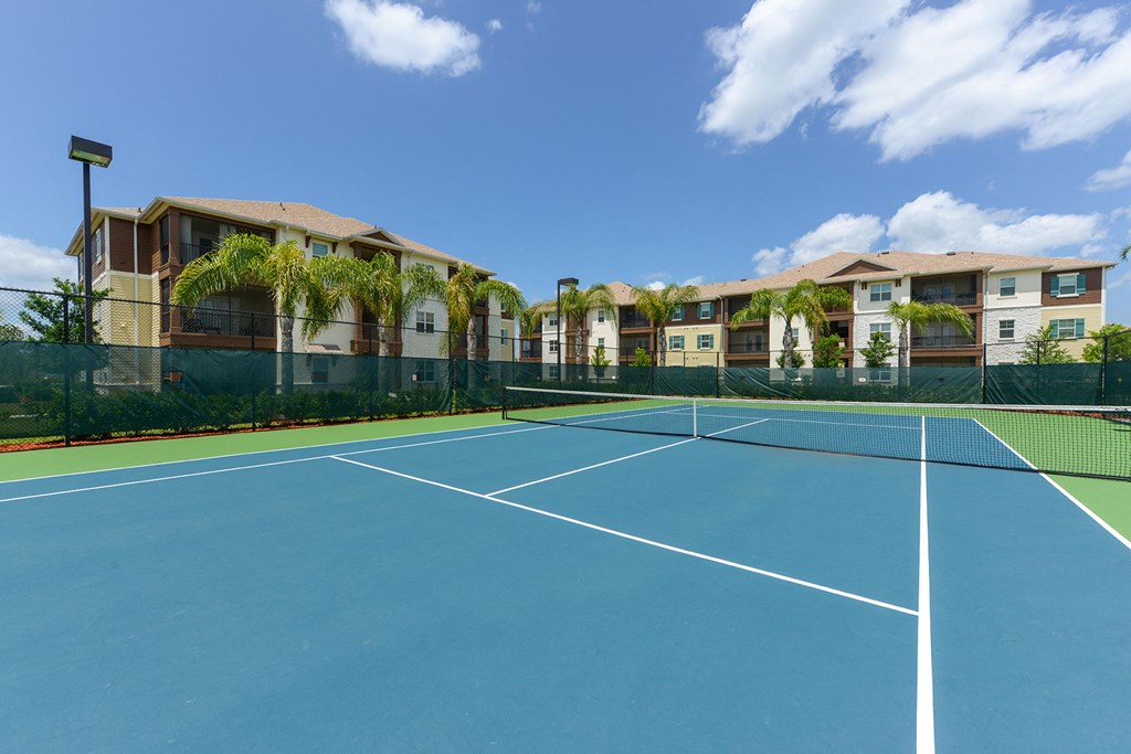 A tennis court is surrounded by a green fence and apartment buildings at Cabana Club Apartments, Florida 32256