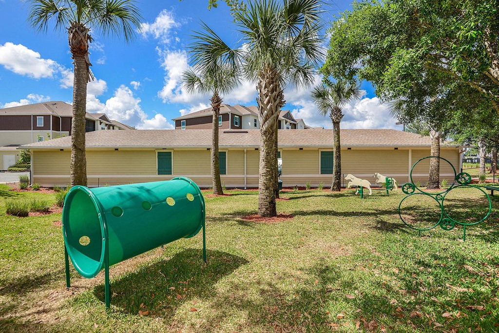 A green cylindrical object is in the foreground of a grassy area with palm trees and a building in the background at Cabana Club Apartments, Jacksonville, FL