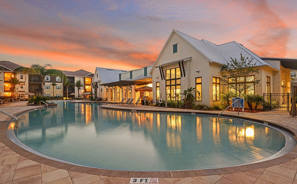 A large swimming pool in front of a building with a sunset in the background at Cabana Club Apartments, Jacksonville, FL
