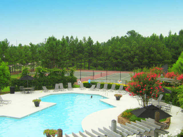 a large pool with chairs around it and a tennis court in the background