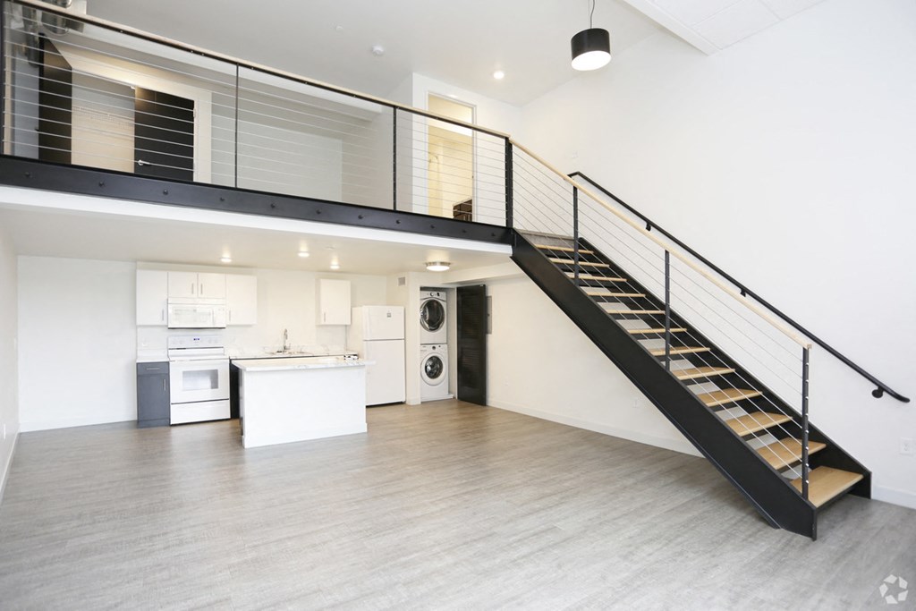 a living room with a staircase and a white kitchen