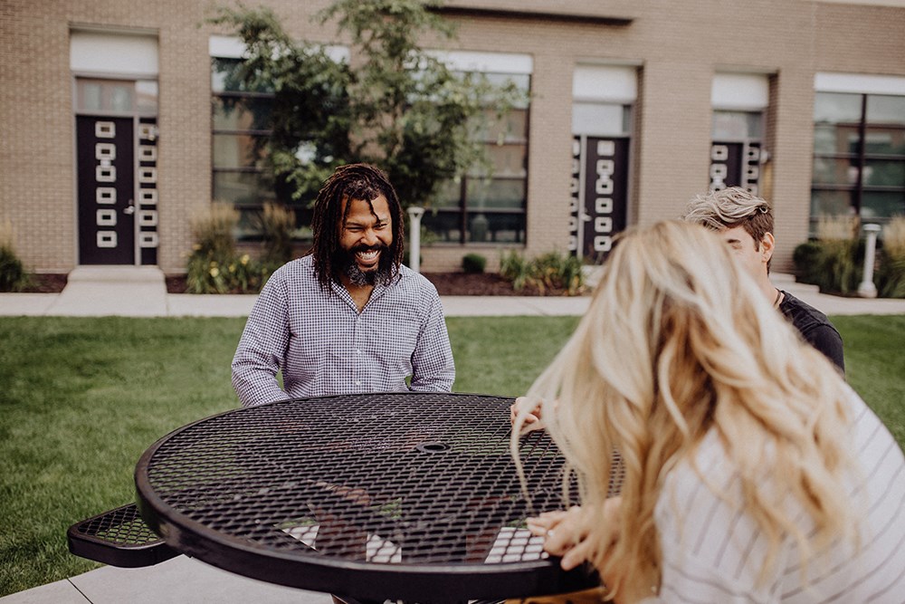 a group of people sitting around a round barbecue grill