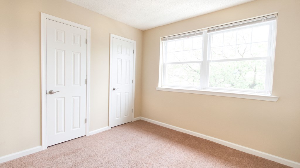 an empty bedroom with two doors and a window