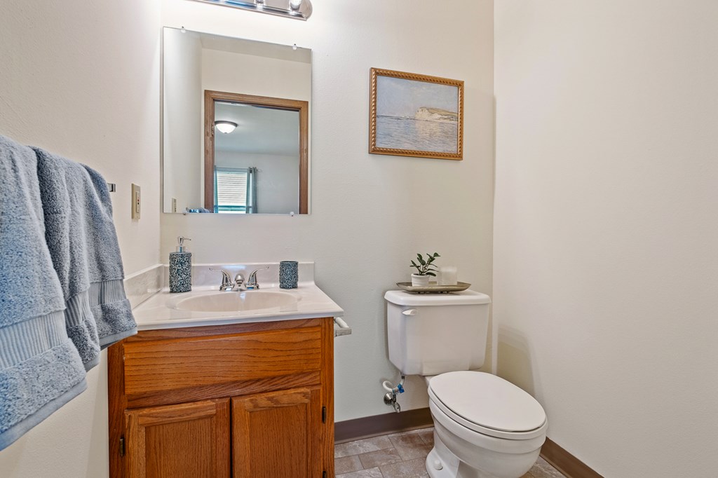 A bathroom with a toilet, sink, mirror, and a picture on the wall.
