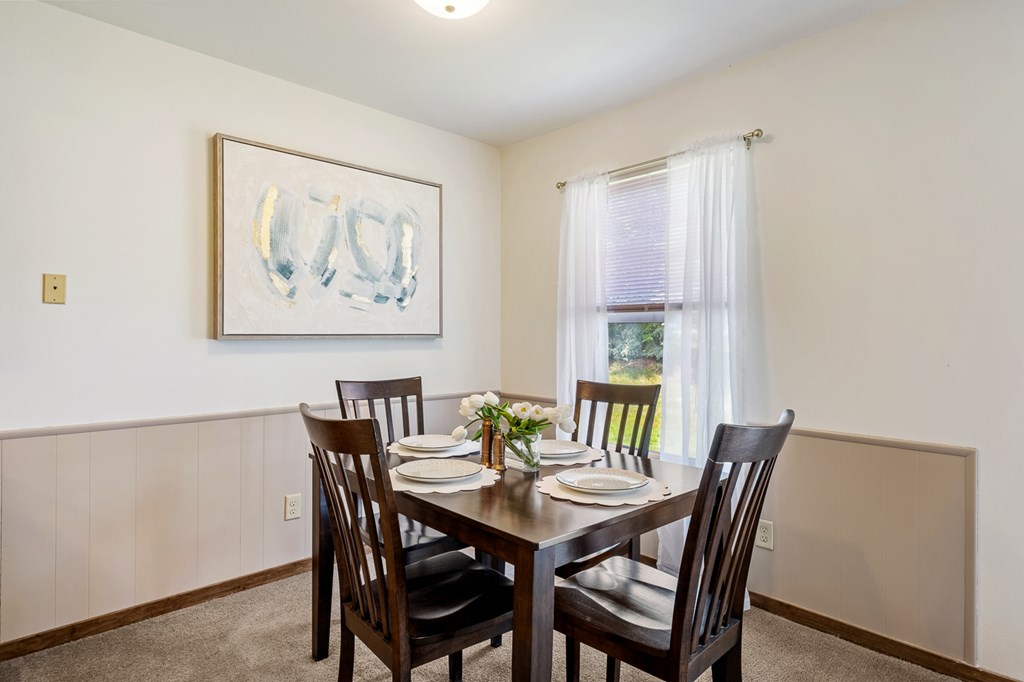 A dining room with a table set for two and a painting on the wall.
