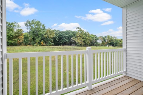 A white deck with a white railing overlooking a grassy field.