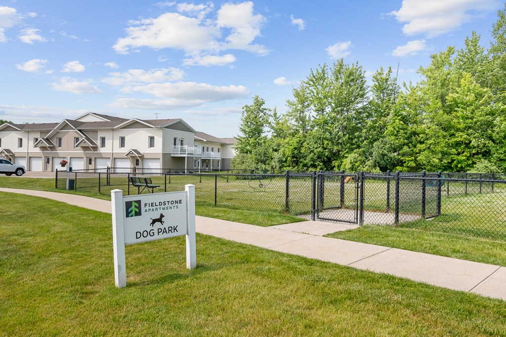 A sign for a dog park in front of a chain link fence.