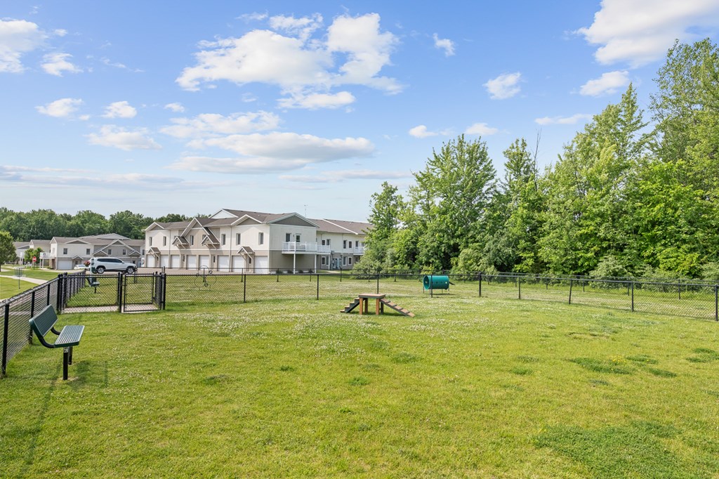 A grassy field with a playground and houses in the background.