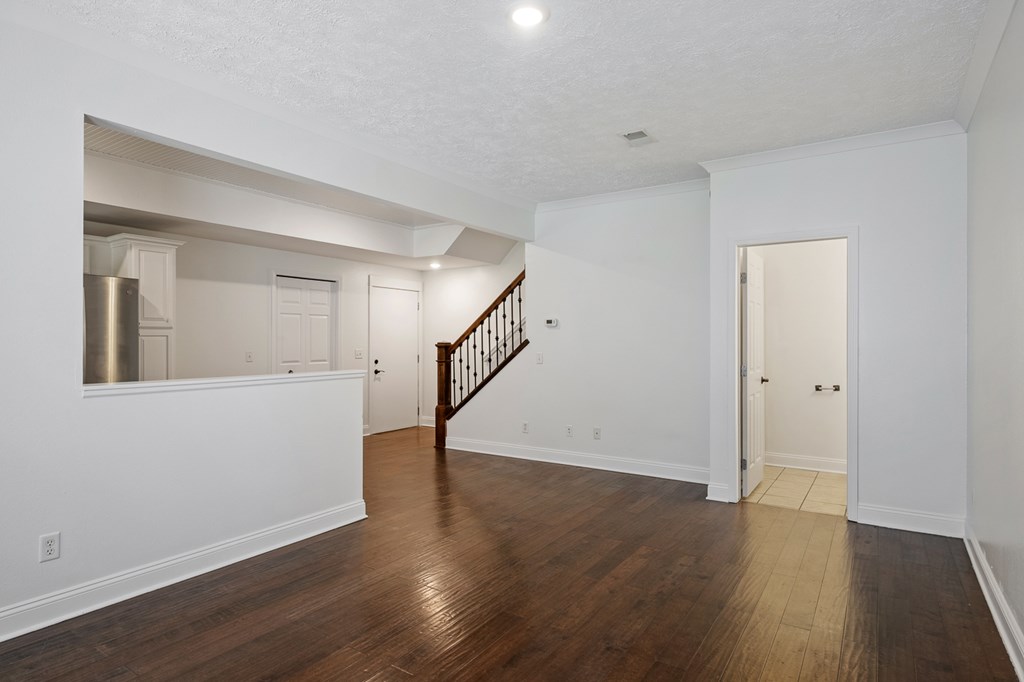 A spacious room with a wooden floor and a staircase.