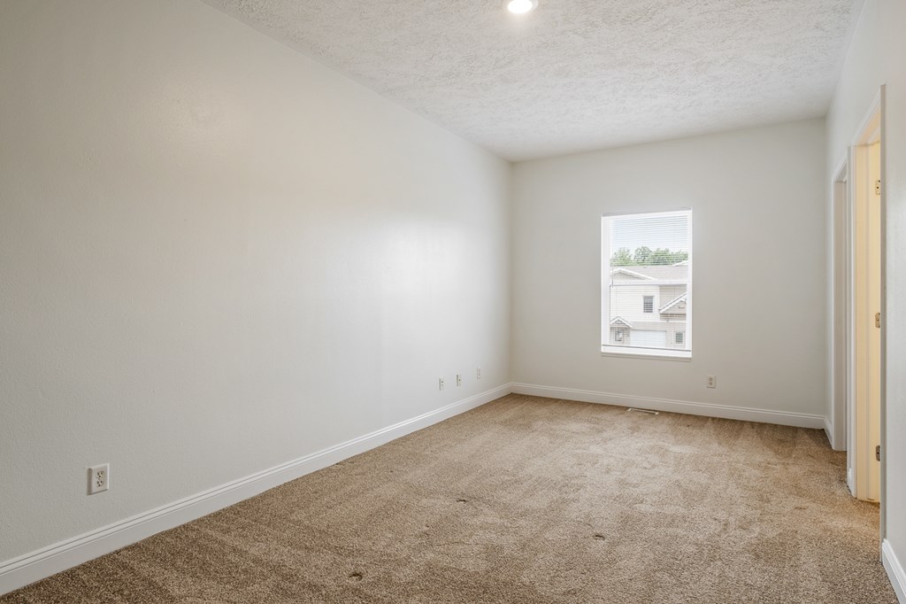 A room with a carpeted floor and a window showing a house.
