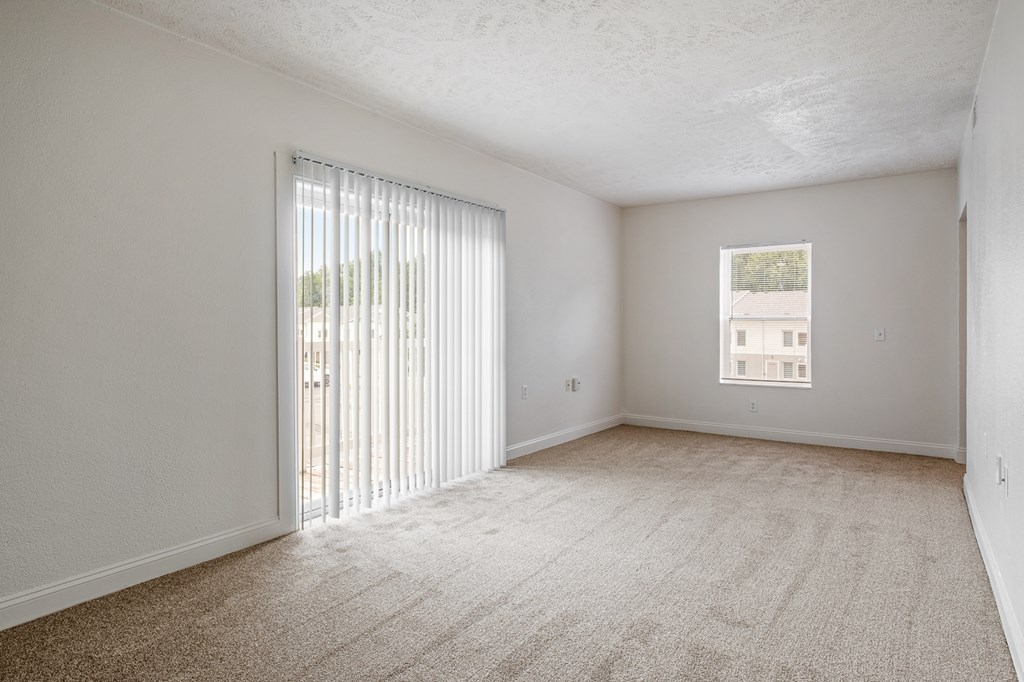 A room with a carpeted floor and a window with blinds.