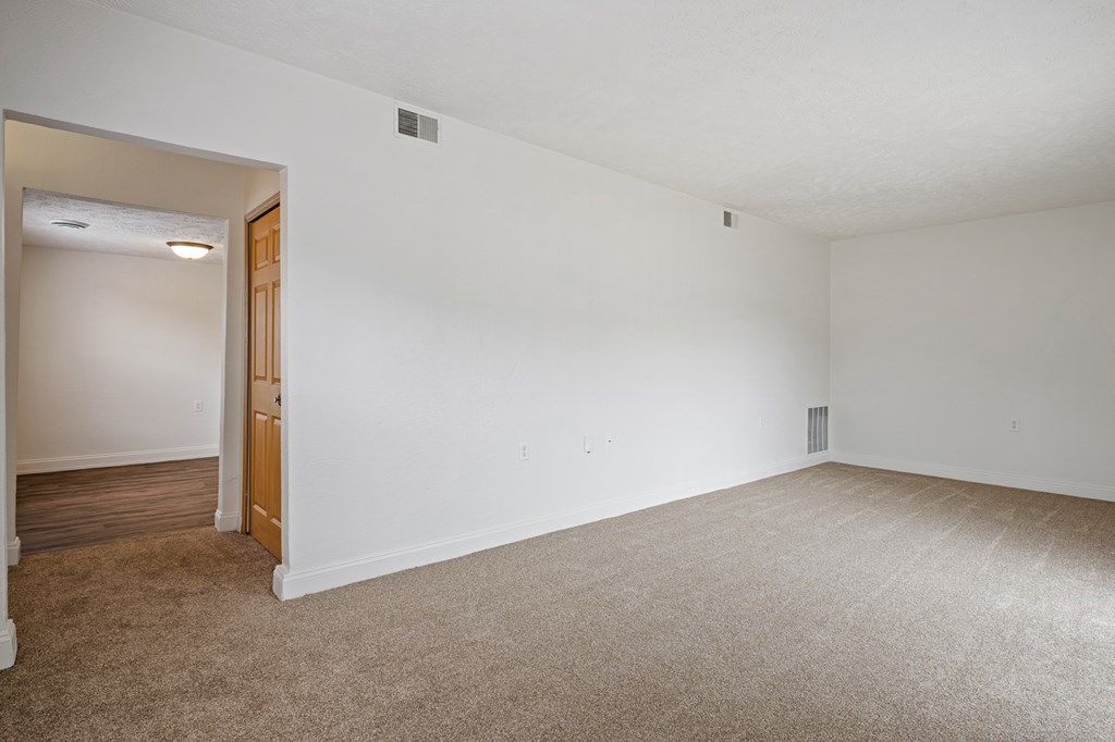 A large, empty room with a carpeted floor and a doorway leading to another room.