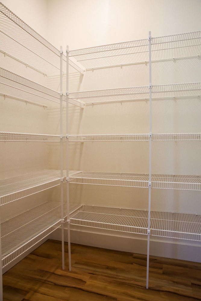 a walk in closet with white metal shelving and a wood floor