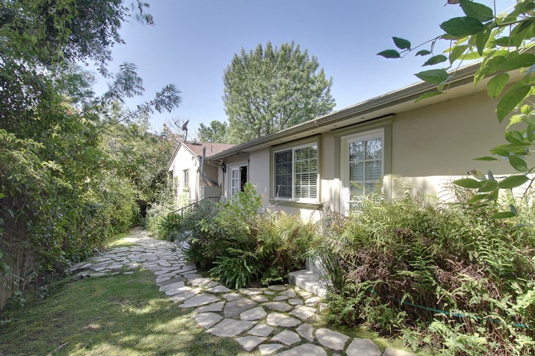 the side of a house with a walkway and plants