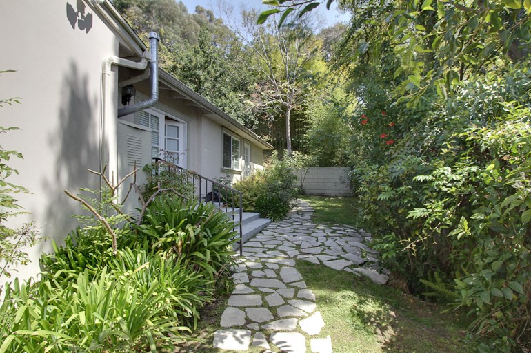 a walkway leading to a white house with a garden and trees