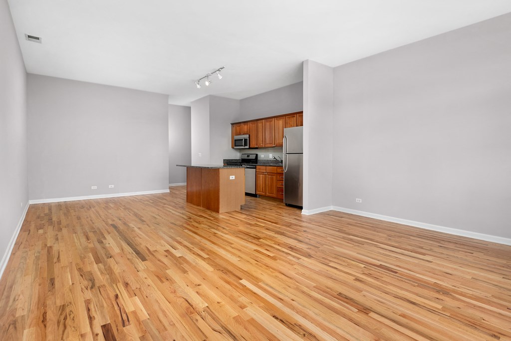 an empty living room with wood floors and a kitchen