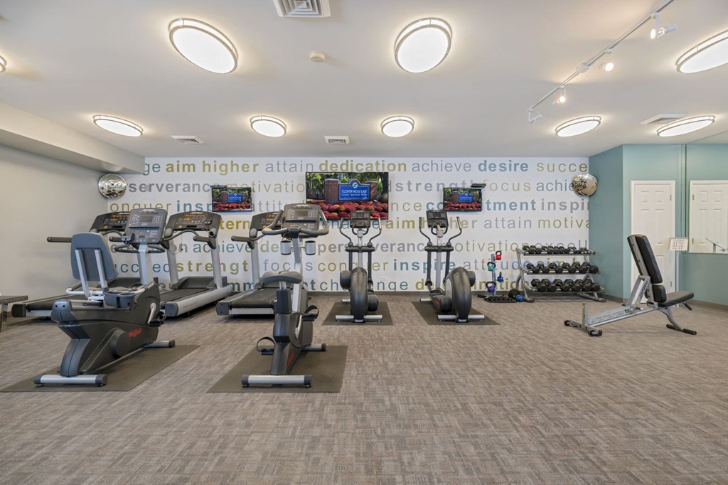 a gym with weights and cardio machines and a wall with a quote